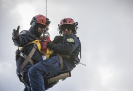 Two National Guard team members dangle from a cable below a helicopter